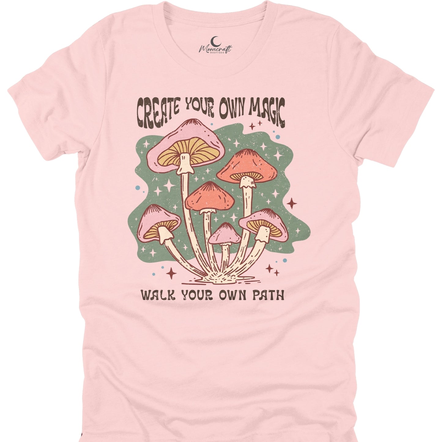 Pink t-shirt with mushroom graphic and text 'Create Your Own Magic, Walk Your Own Path' on a white background