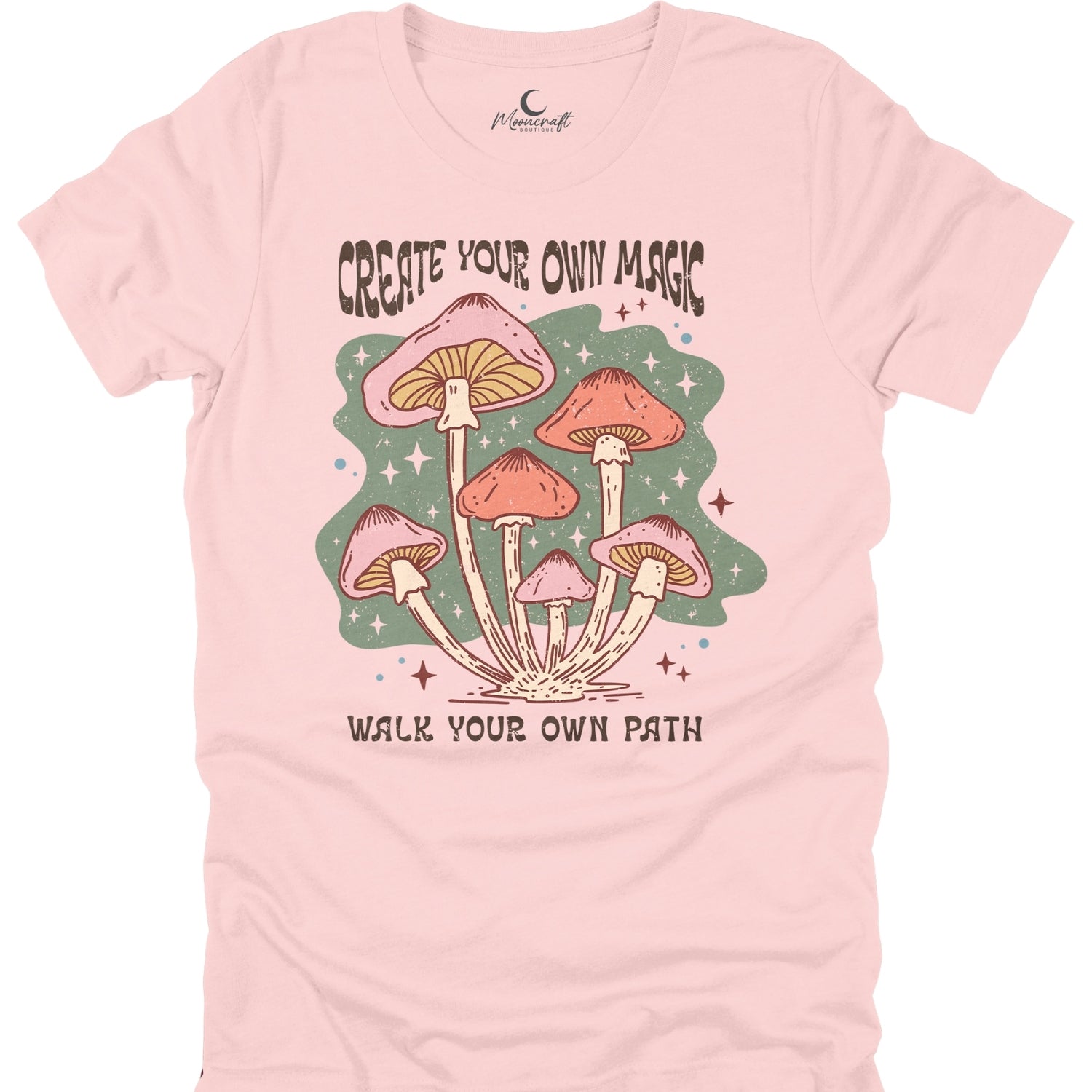 Pink t-shirt with mushroom graphic and text 'Create Your Own Magic, Walk Your Own Path' on a white background