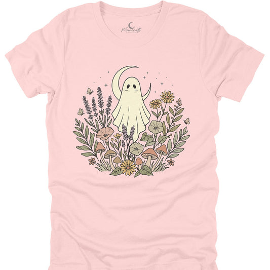 A light pink short-sleeve t-shirt with a central graphic of a cute cartoon ghost surrounded by wildflowers, a crescent moon, and small butterflies. The brand name 'Peachy Soft' is printed inside the collar.