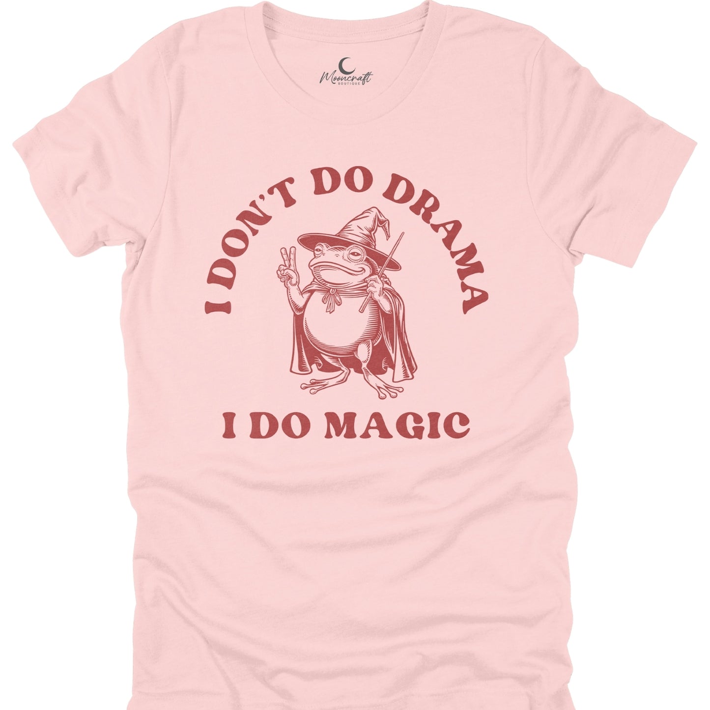 Pink t-shirt with a graphic of a frog in a witch hat and cape, text 'I Don't Do Drama I Do Magic', and a brand logo on a white background.