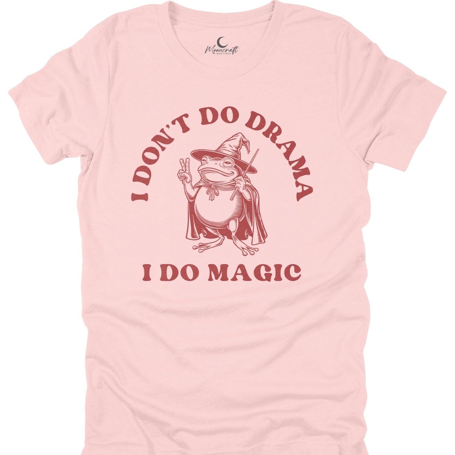 Pink t-shirt with a graphic of a frog in a witch hat and cape, text 'I Don't Do Drama I Do Magic', and a brand logo on a white background.
