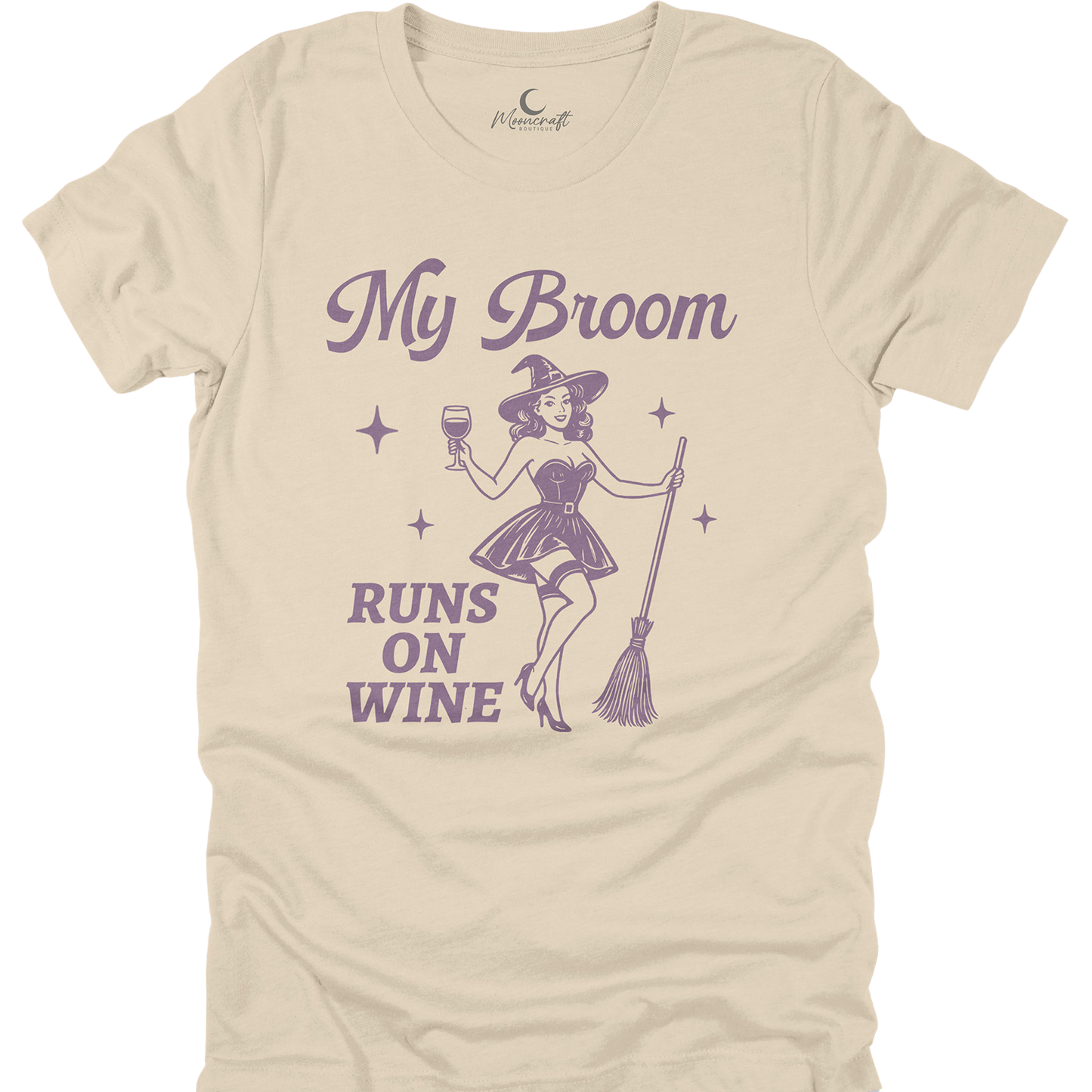 Beige t-shirt with purple graphic of a witch holding a broom and wine glass, and text 'My Broom Runs on Wine'.