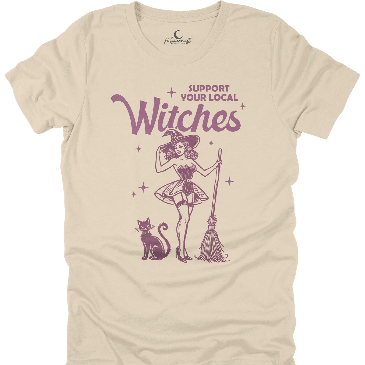 Beige t-shirt with a graphic of a witch, cat, and broomstick, and text 'Support Your Local Witches' on a white background.