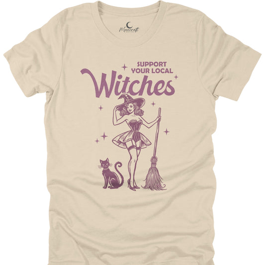 Beige t-shirt with a graphic of a witch, cat, and broomstick, and text 'Support Your Local Witches' on a white background.
