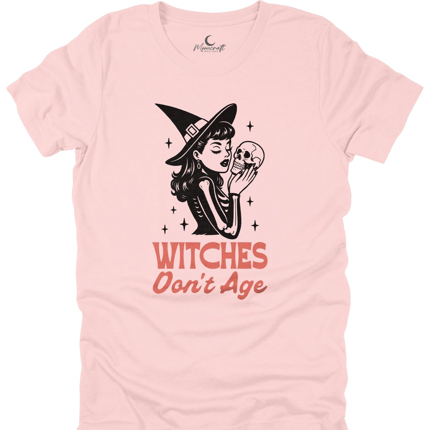 Pink t-shirt with a graphic of a witch holding a skull and text 'Witches Don't Age' on a white background.