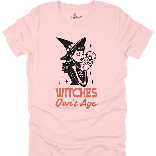Pink t-shirt with a graphic of a witch holding a skull and text 'Witches Don't Age' on a white background.